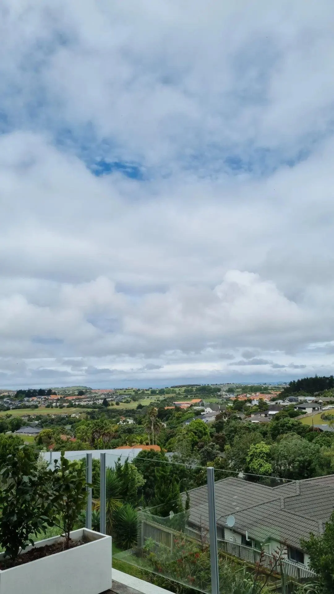 View of a suburban landscape with houses, trees, and rolling hills under a cloudy sky.