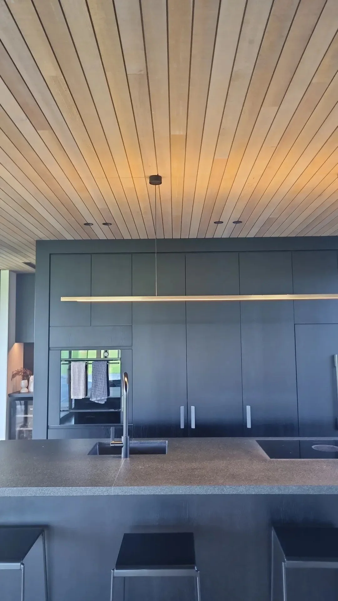 Modern kitchen with black cabinetry, a black countertop, a sink with a faucet, and a wooden ceiling with recessed lighting.