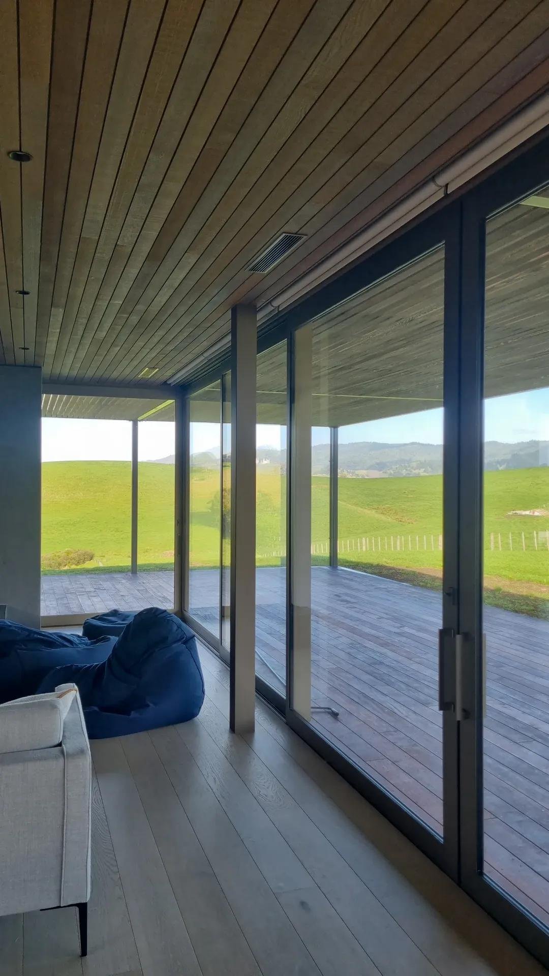 Interior of a modern house with large glass sliding doors opening to a grassy outdoor landscape with hills in the distance.