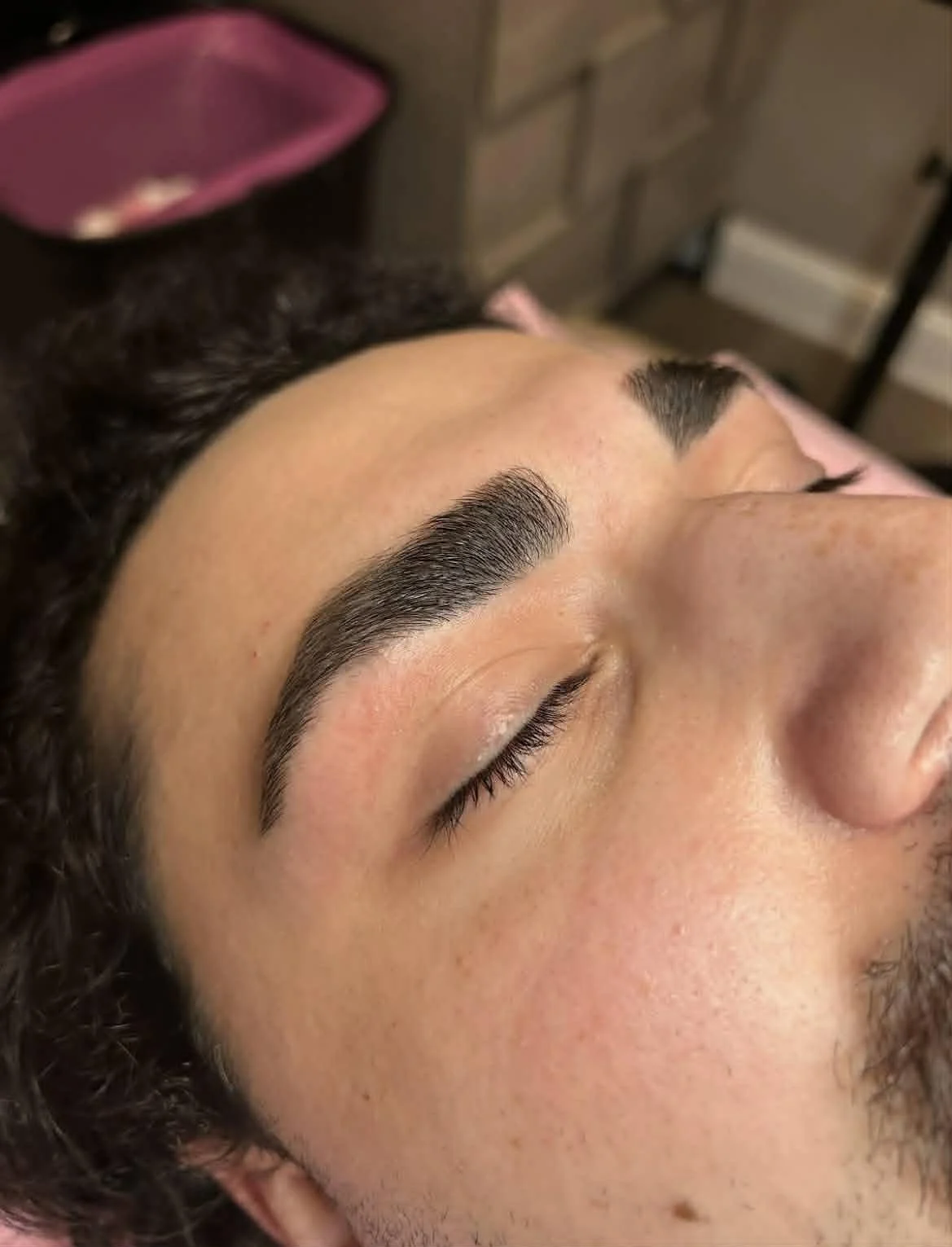 Close-up of a person's face with freshly groomed eyebrows, lying down with eyes closed.