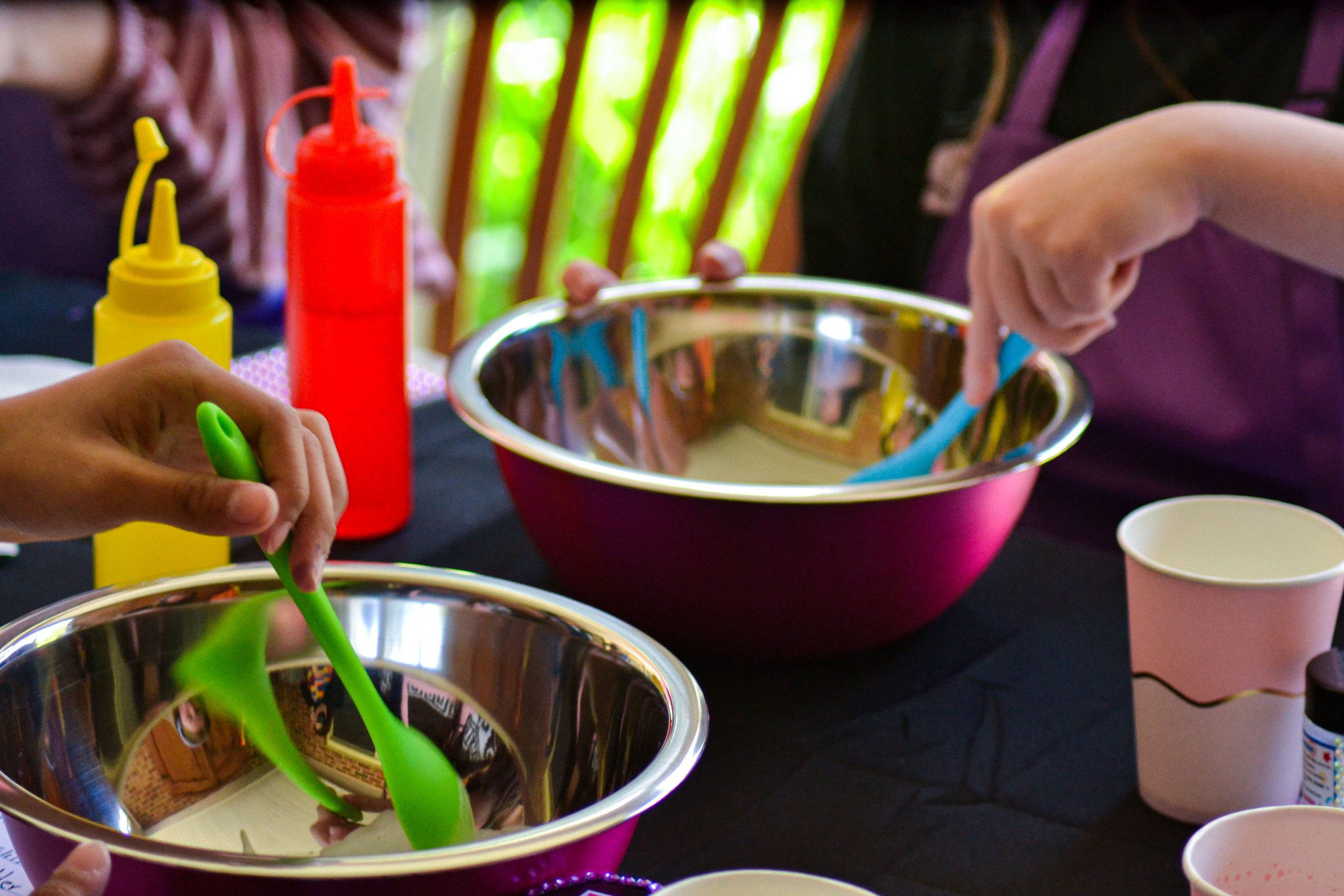 Kid's mixing slime in shiny bowls with colourful spoons.