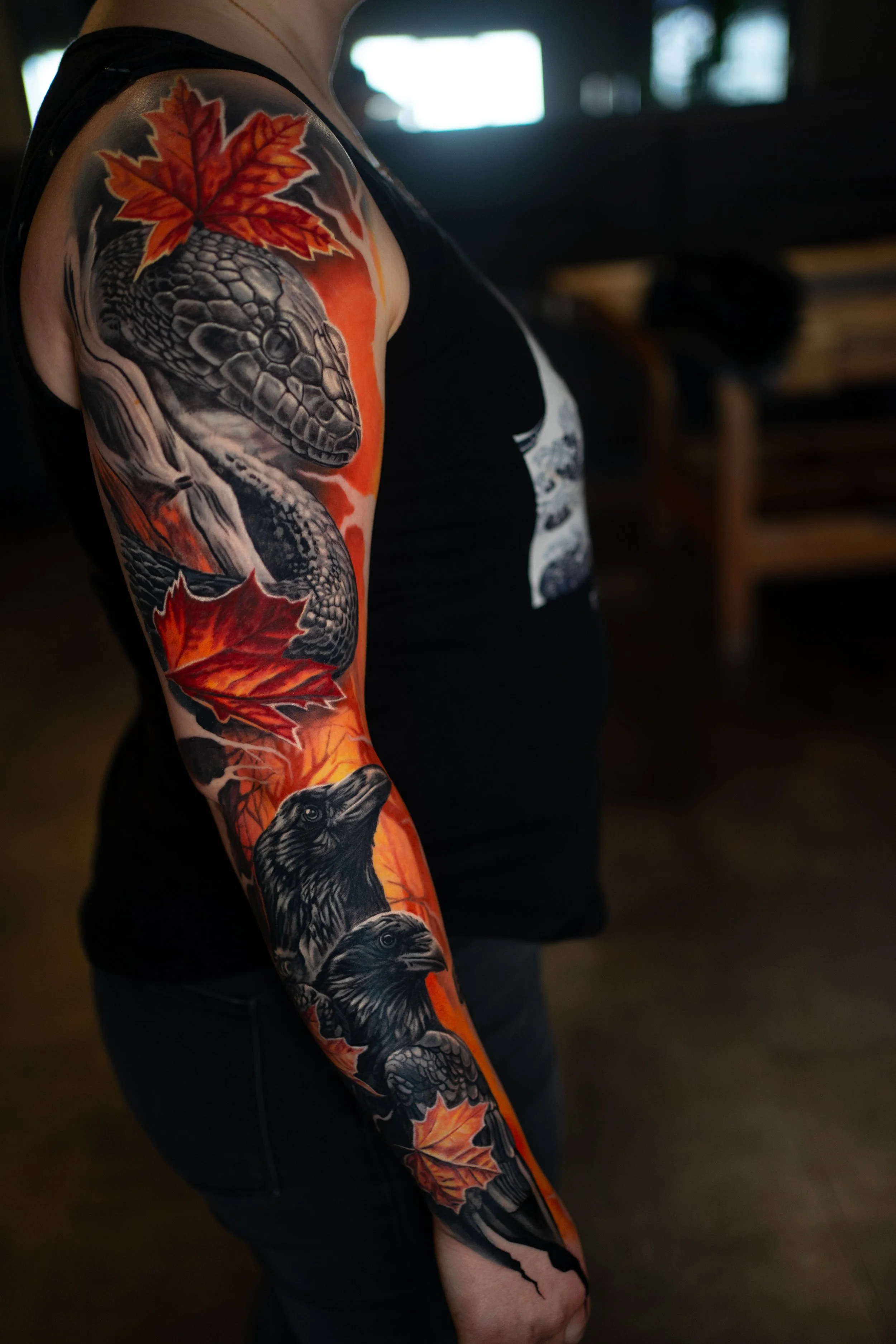 Tattoo auf dem Arm einer Person mit einem Löwenkopf, mehreren roten Ahornblättern und einem schwarzen Vogel.