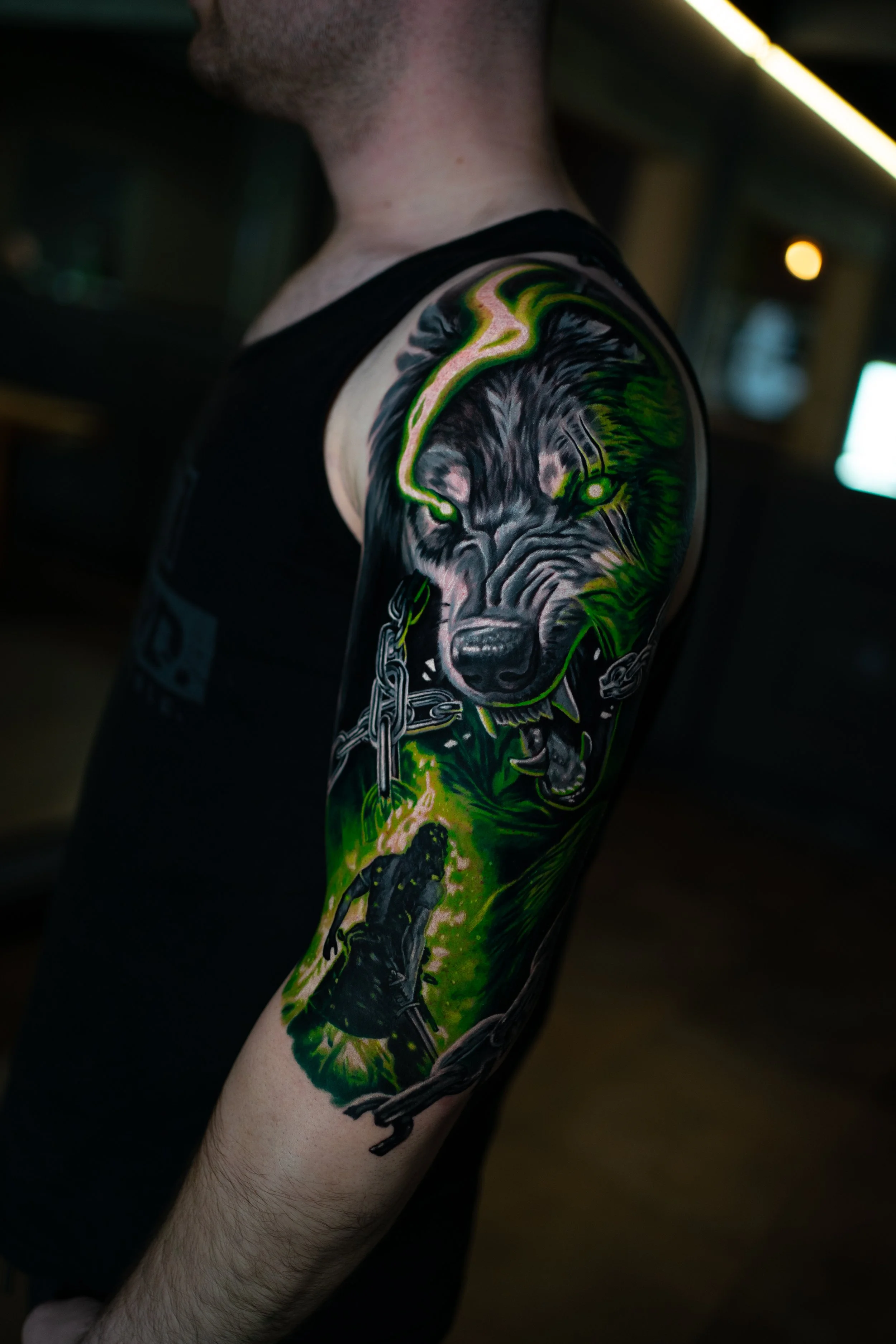 Tattoo eines Wolfes, das auf dem Oberarm eines Mannes tätowiert ist, mit grünen und schwarzen Farben.