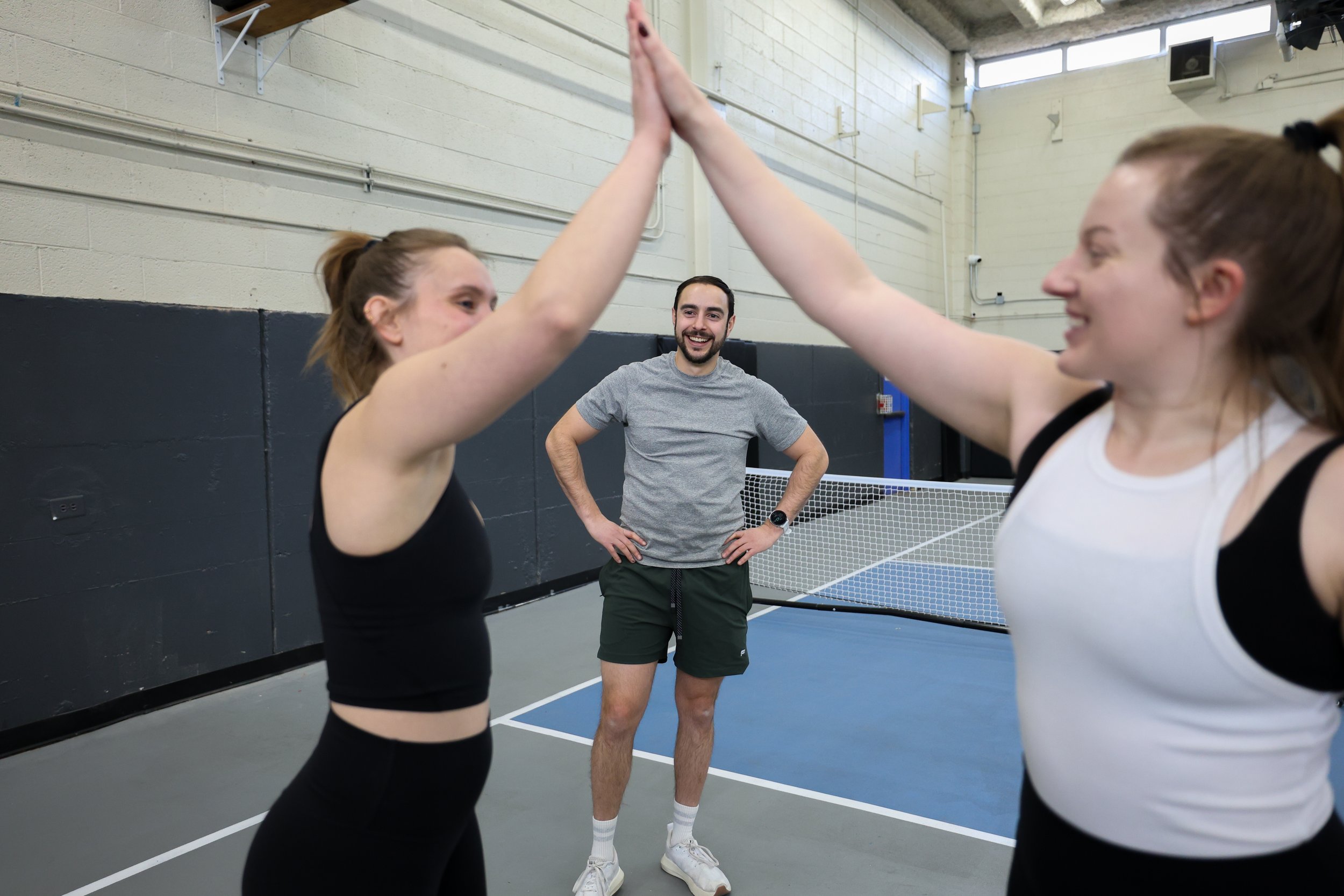 two women high five after finishing a partner workout. coach stands in the background smiling.
