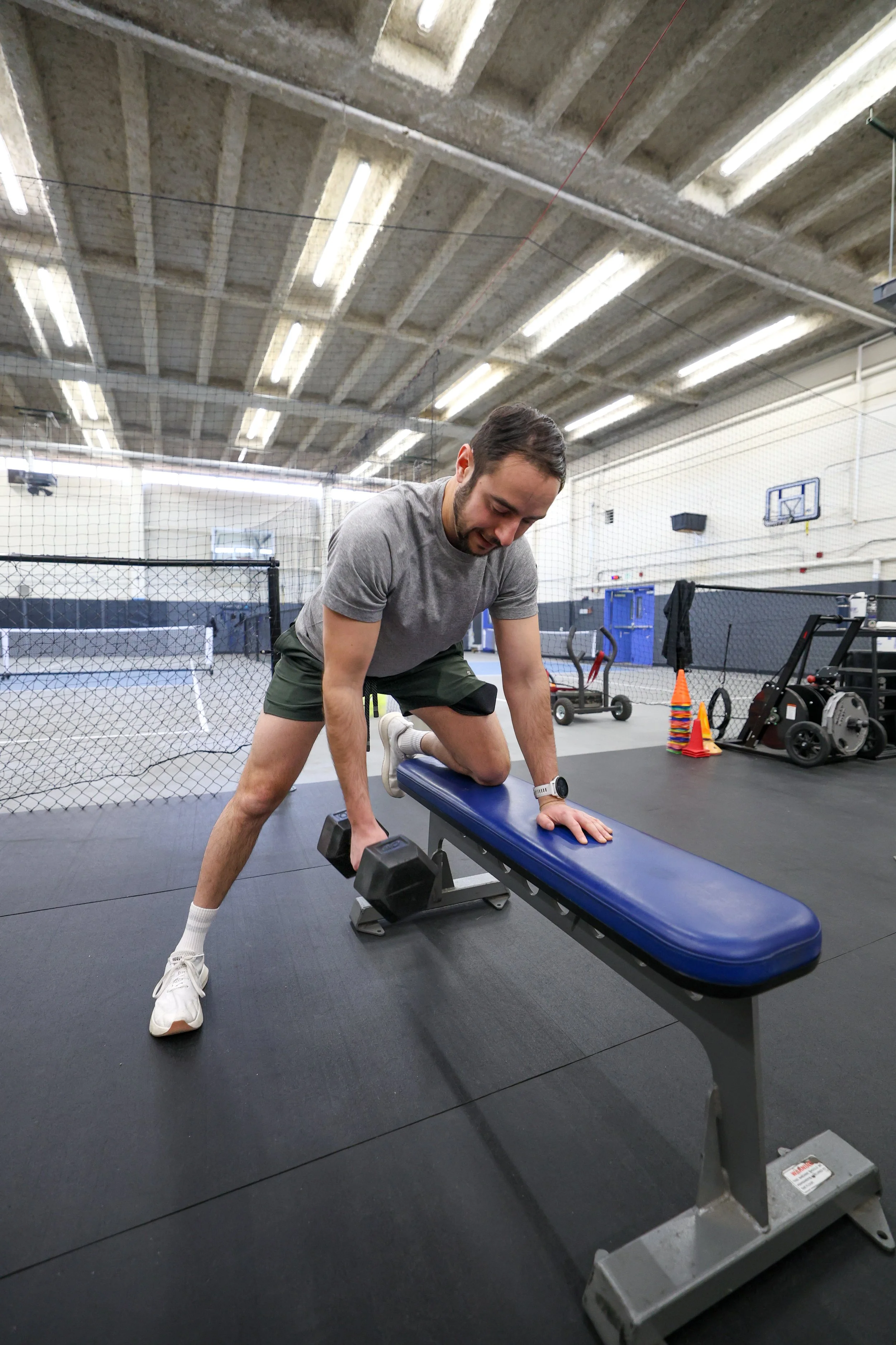 Man doing 3 point bent over row with left hand and left knee on a workout bench and right arm pulling the weight