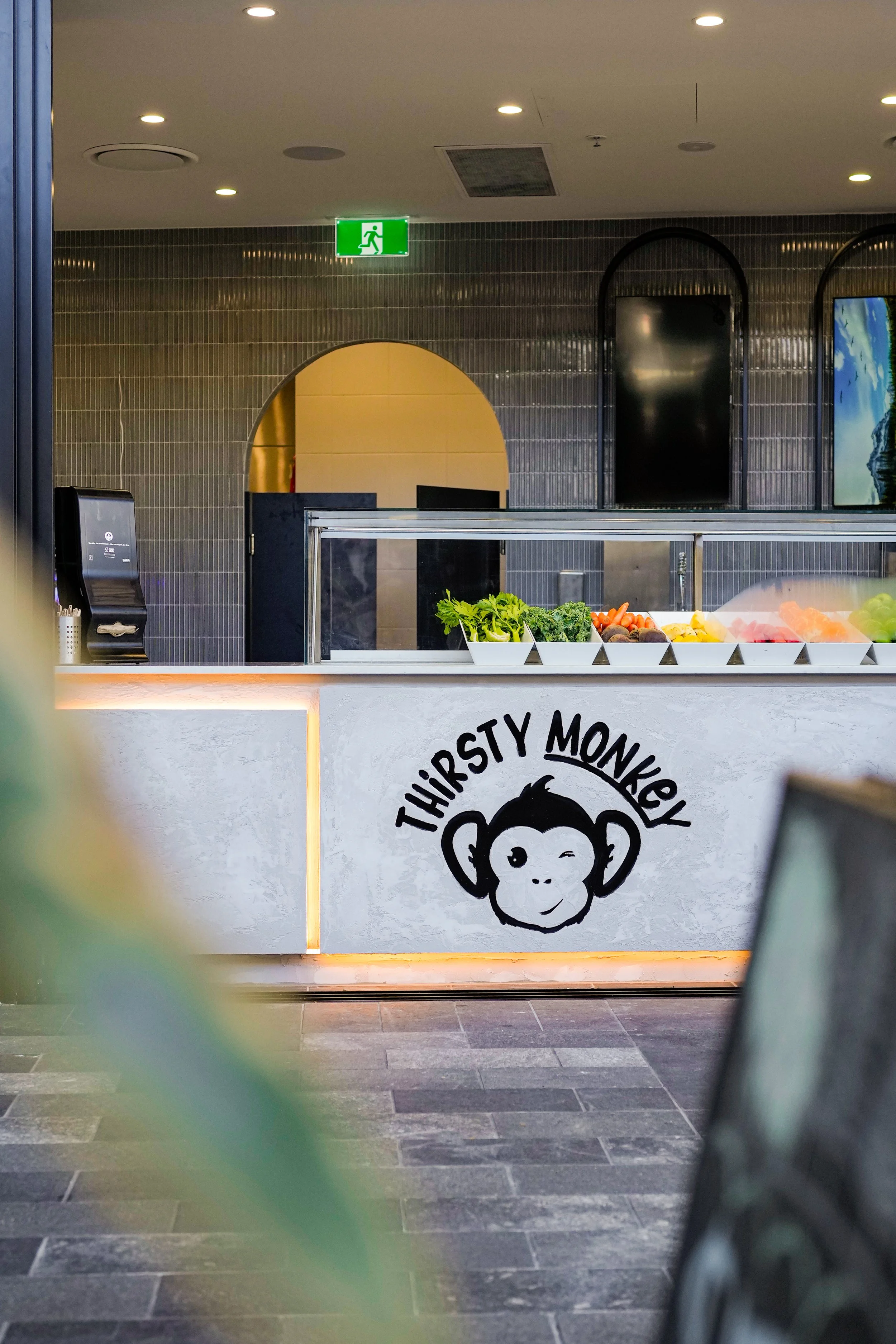 Counter at a Thirsty Monkey store with colourful fruits on display, located in a shopping mall or food court.