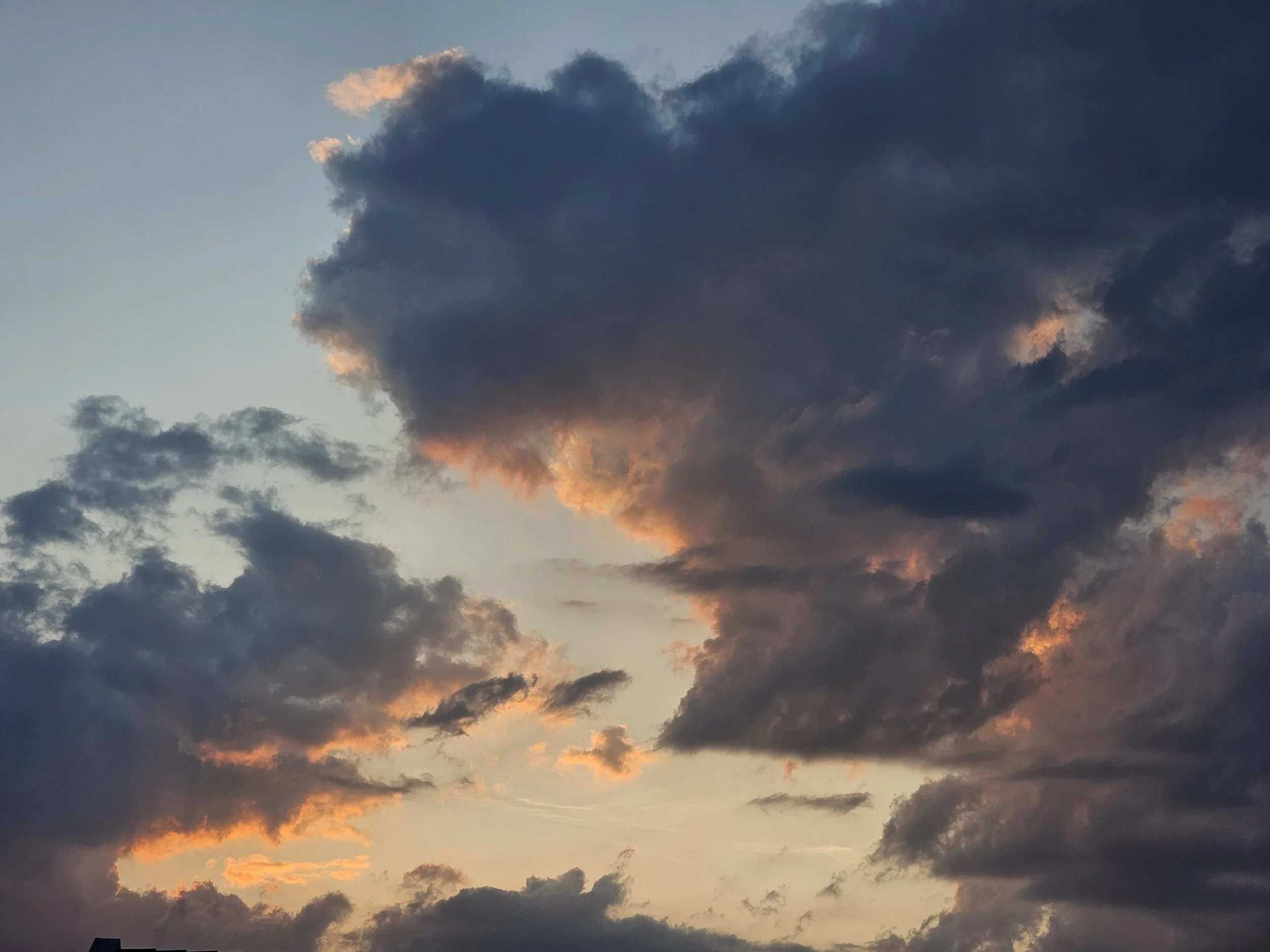 A dramatic shot of deep gray clouds illuminated from beneath by a warm orange glow during sunset.