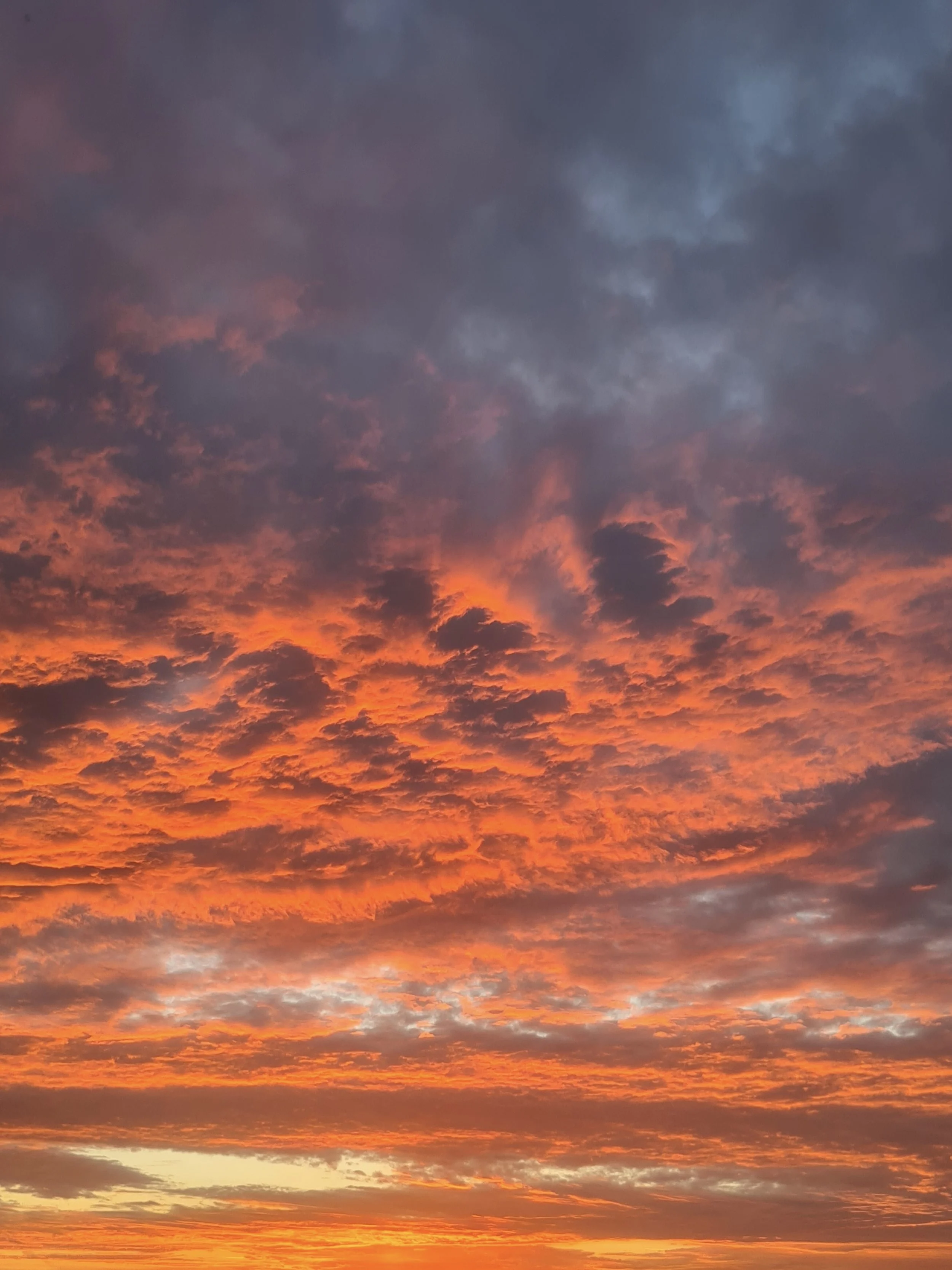 A wide shot of a sunset sky featuring intense orange and red clouds beneath a layer of dark, contrasting stormy gray clouds.