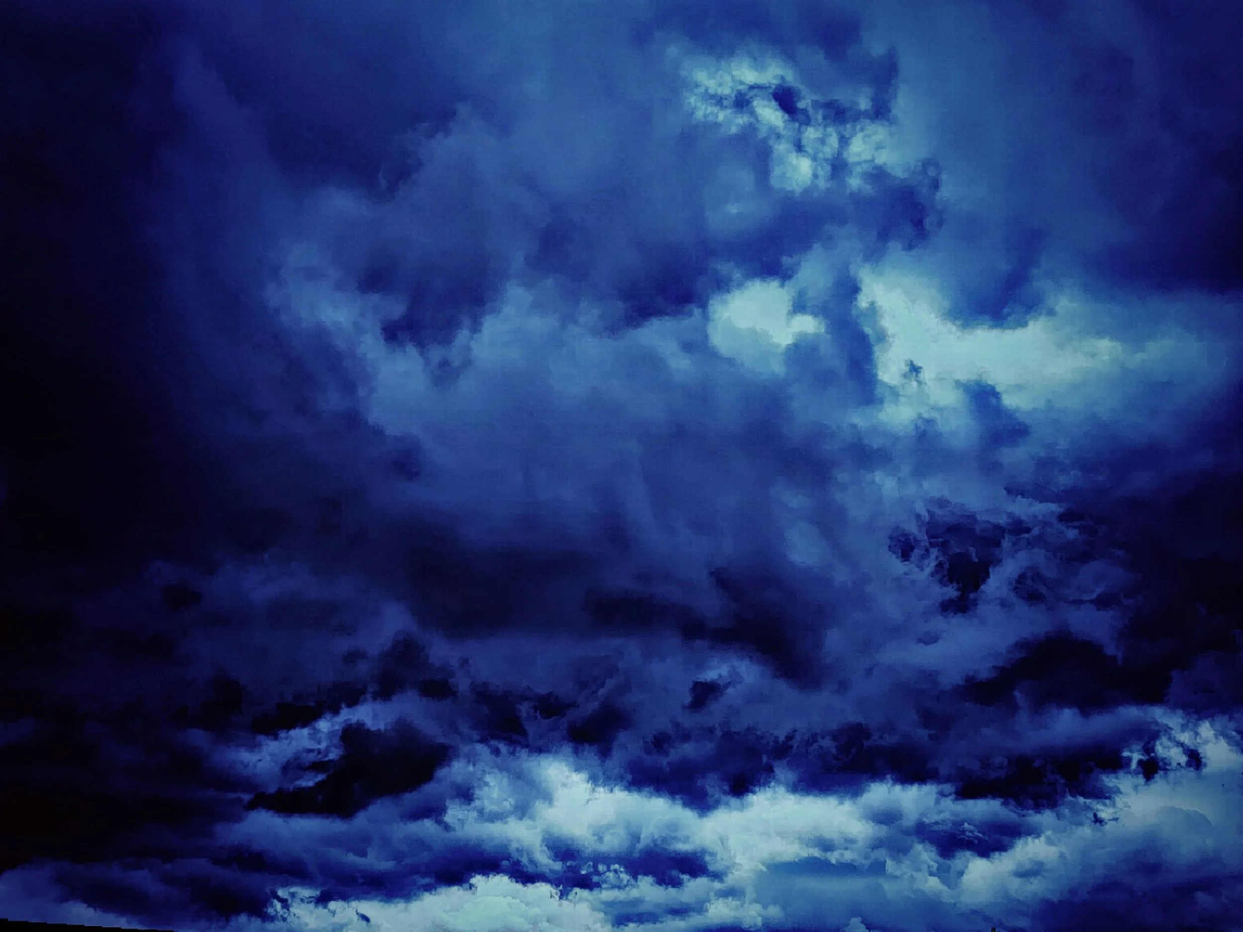 A high-contrast, moody photograph of a dark blue stormy sky with deep shadows and heavy cloud textures.