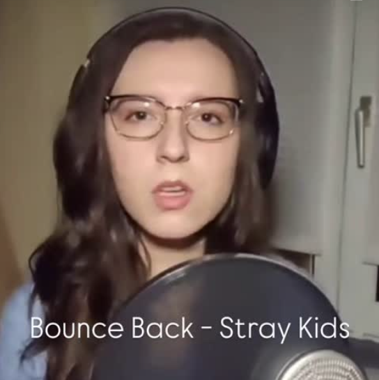 Artist sandra spirou singing a cover of the song Bounce Back by the band Stray Kids. The image shows her in a room with a window, white blinds and a light brown curtain.