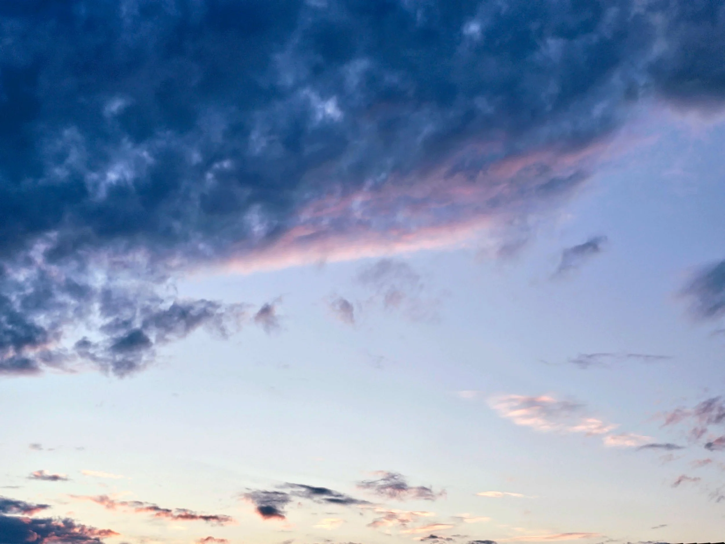 A soft blue evening sky scattered with light clouds, highlighted by a subtle streak of pink light.