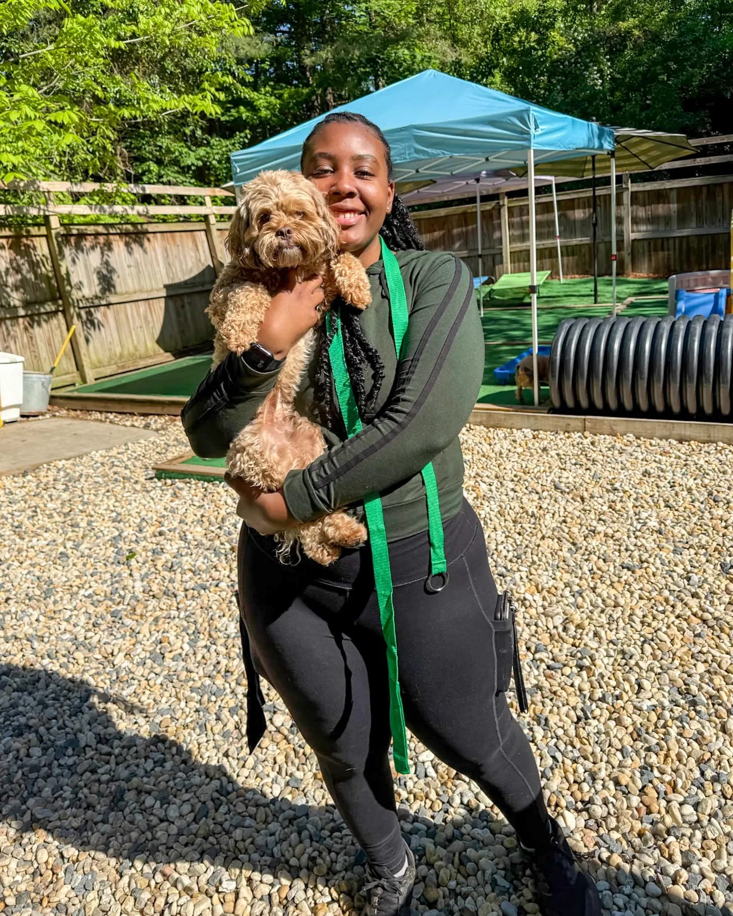 A photo of a smiling young woman wearing a green shirt and black leggings, holding a small white dog.