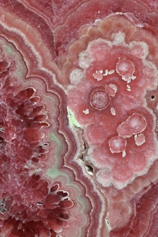 Close-up of a polished pink, red, and white mineral or gemstone with layered bands and crystalline structures.