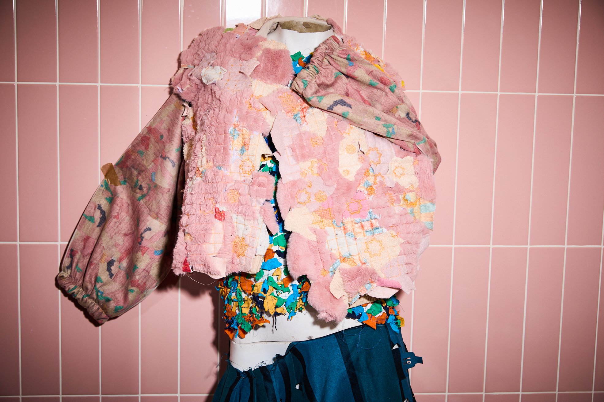 a mannequin wearing a faux fur jacket, pink tiles in the background