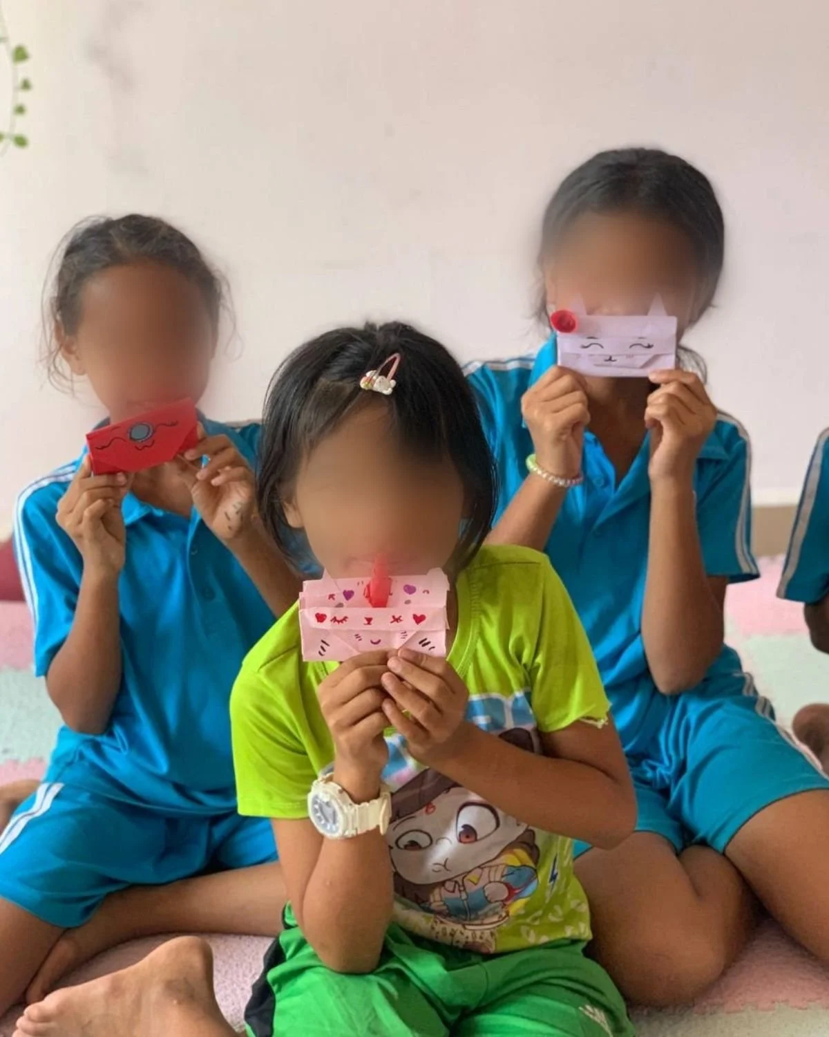 Three girls are sitting together, each holding decorated paper crafts