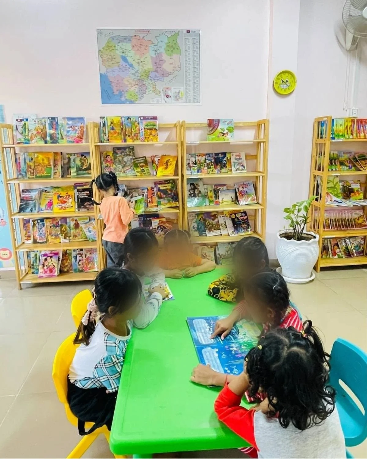 Children sitting around a green table in a library, reading books