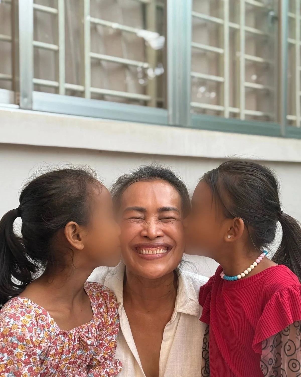 Somaly smiling with two young girls giving her kisses on the cheeks.