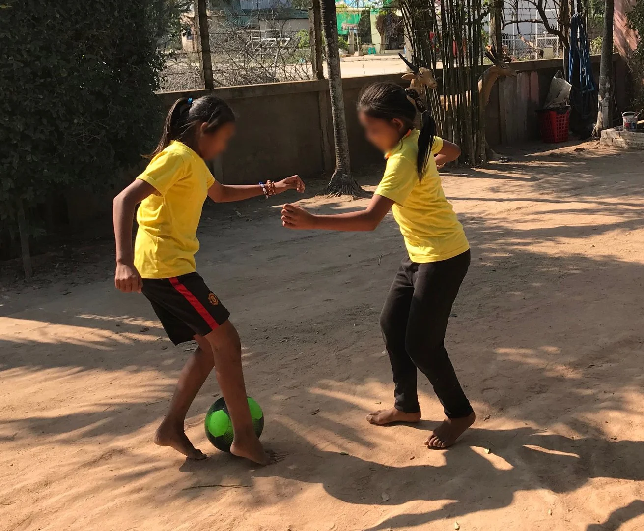 Two young girls playing  soccer barefoot outside