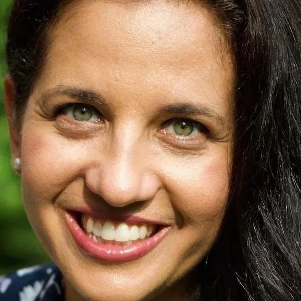 Close-up of a woman smiling with green eyes, dark hair, and a shiny complexion.