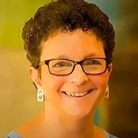 A smiling woman with short curly hair, glasses, and earrings.