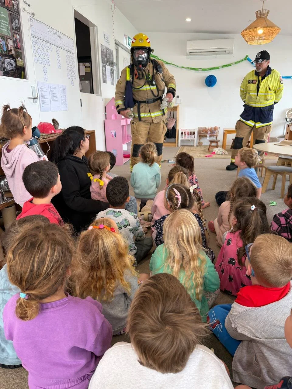 Firefighters giving a safety presentation to a group of young children in a classroom.