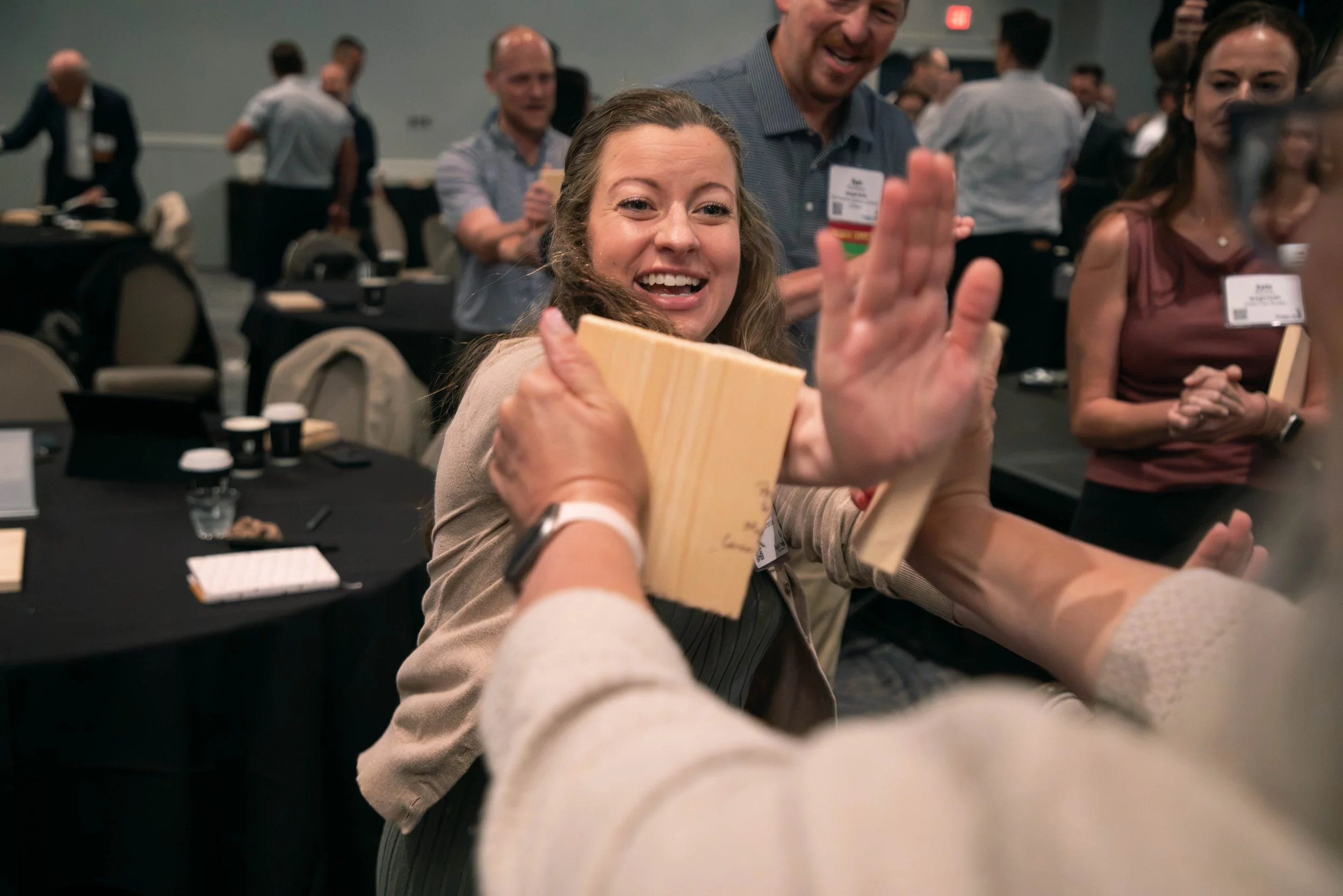 A group of people at a conference happily taking a selfie together, with one woman smiling broadly in the foreground, holding a wooden plaque or award, while others around her are engaged and smiling.