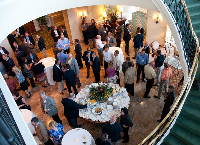 People socializing at a business networking event in a hotel lobby with a buffet table in the center.