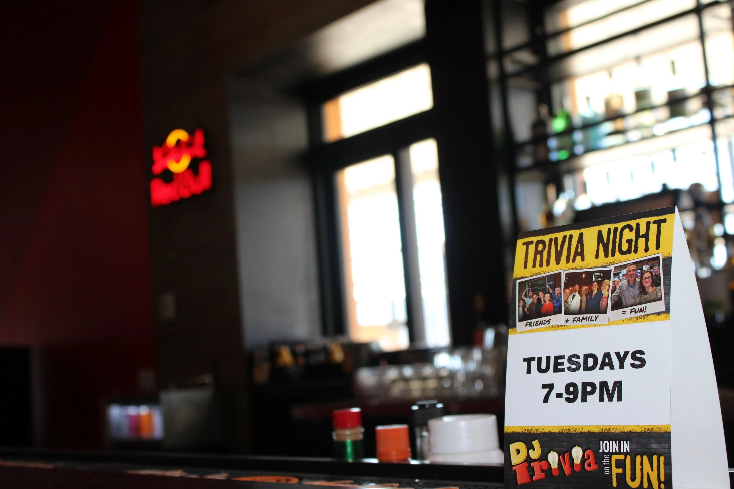 A poster advertising a trivia night with photos of groups of people, indicating it is a fun event for friends and family, held on Tuesdays from 7 to 9 PM.