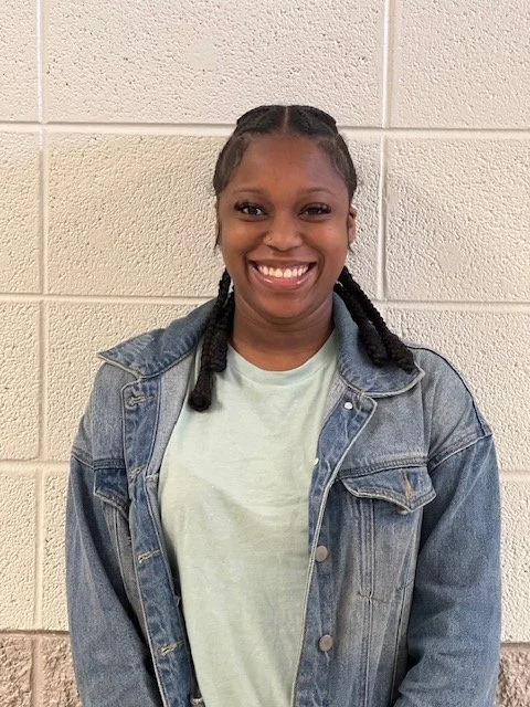 Kayla of Huntsville Behavior Associates with braided hair, wearing a light green shirt and denim jacket against a brick wall.