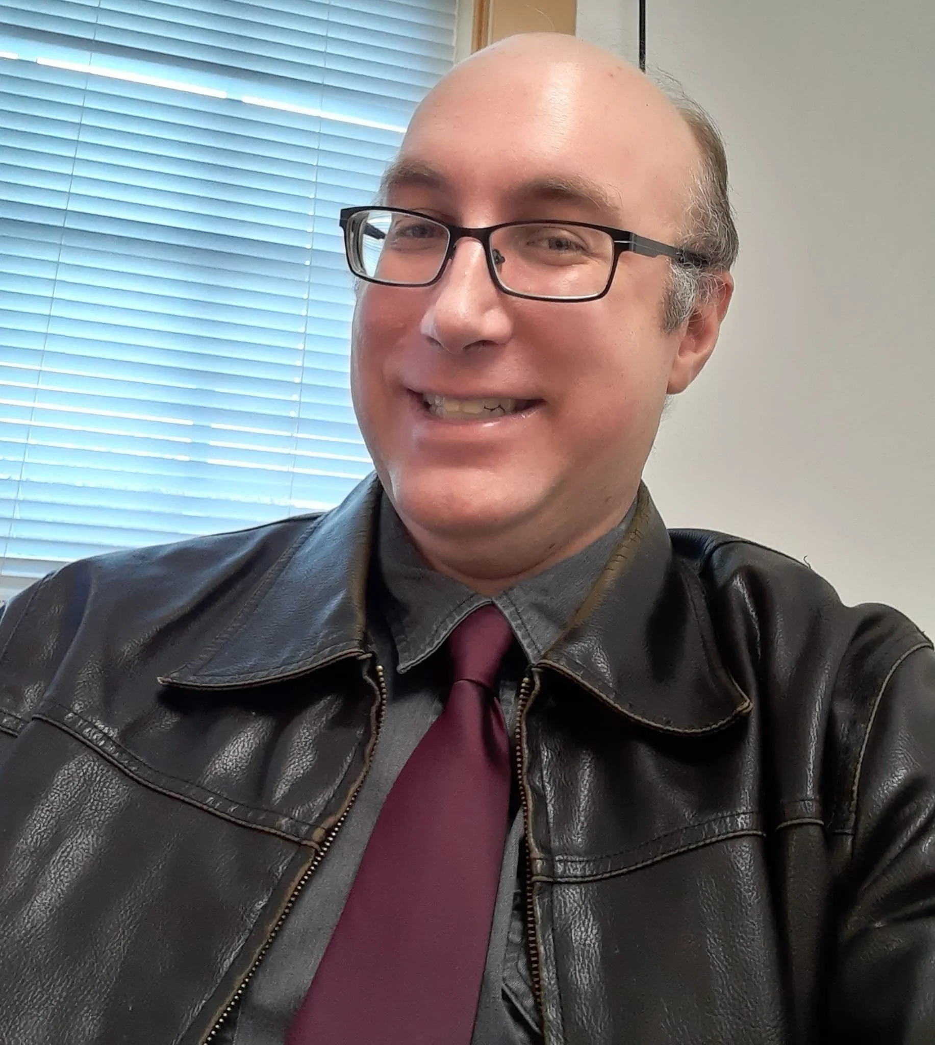 Robert of Huntsville Behavior Associates wearing glasses and a leather jacket, standing indoors near a window.