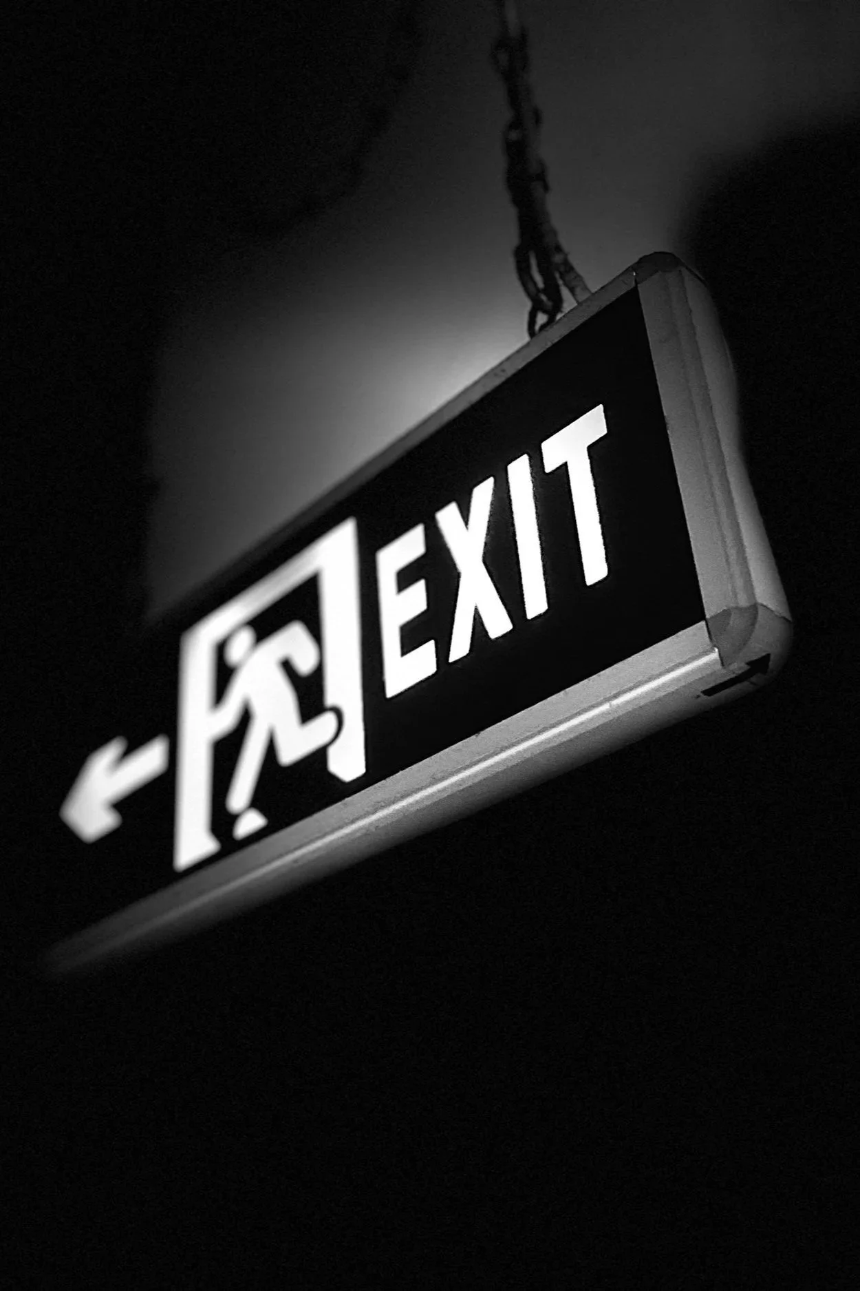 Black and white illuminated exit sign with a person figure pointing to the left.