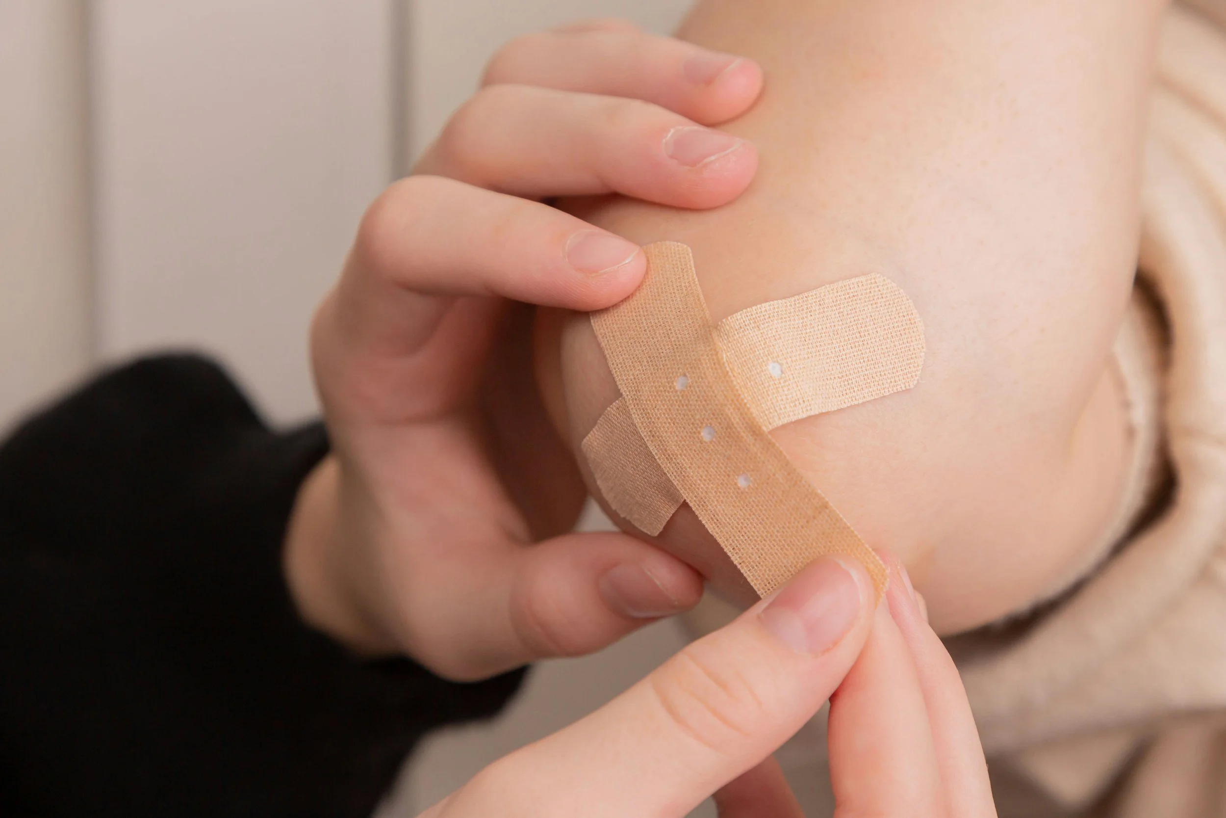 A close-up of a person with a bandage on their arm, using their fingers to peel or adjust the bandage.