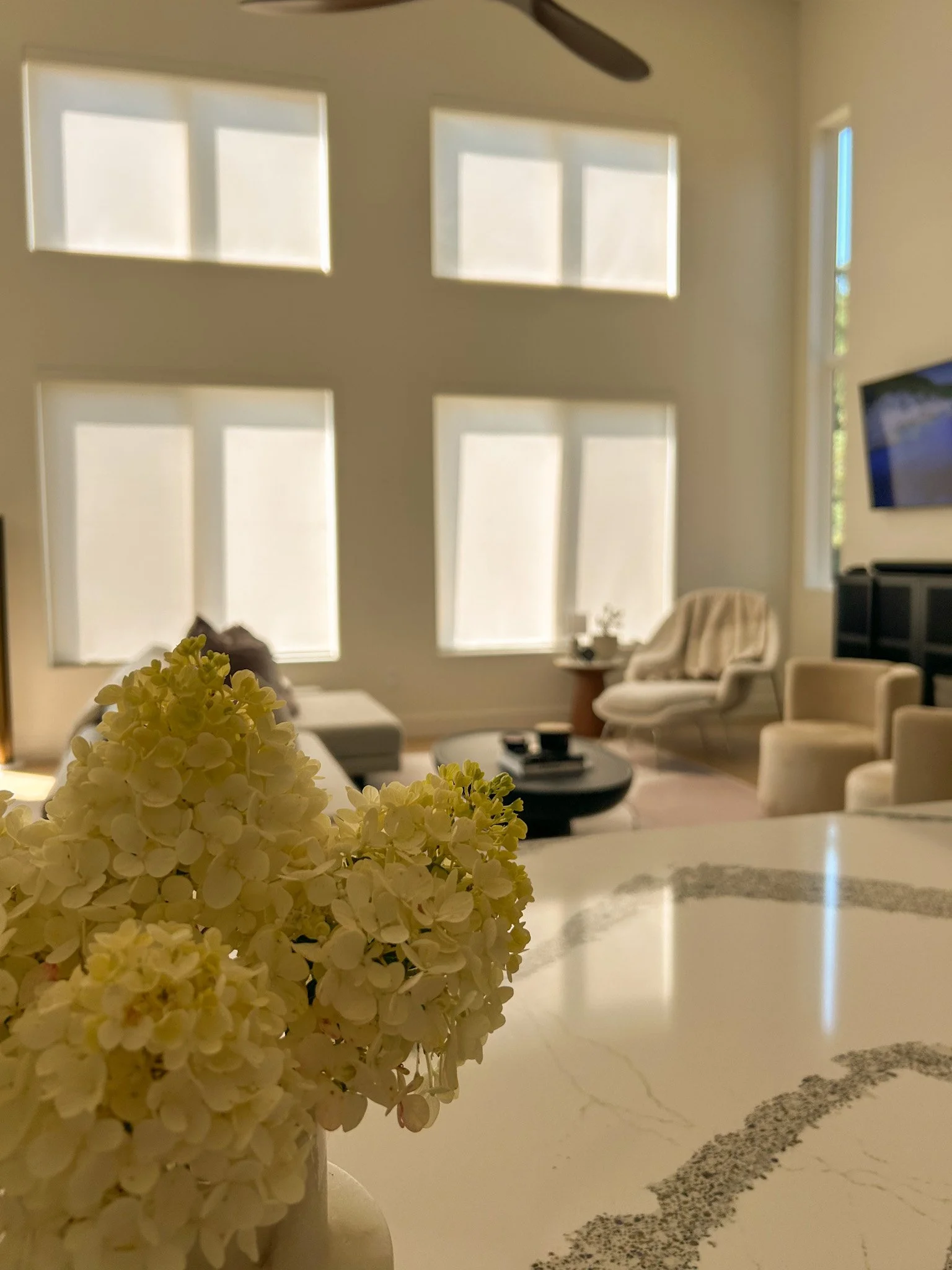 A cozy living room with a neutral-colored sofa and chairs. in the foreground a vase with fresh hydrangeas.