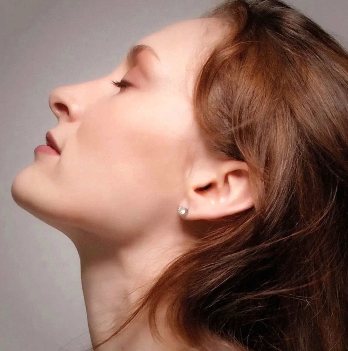 A side profile of a woman with closed eyes, fair skin, red hair, and wearing a small earring.