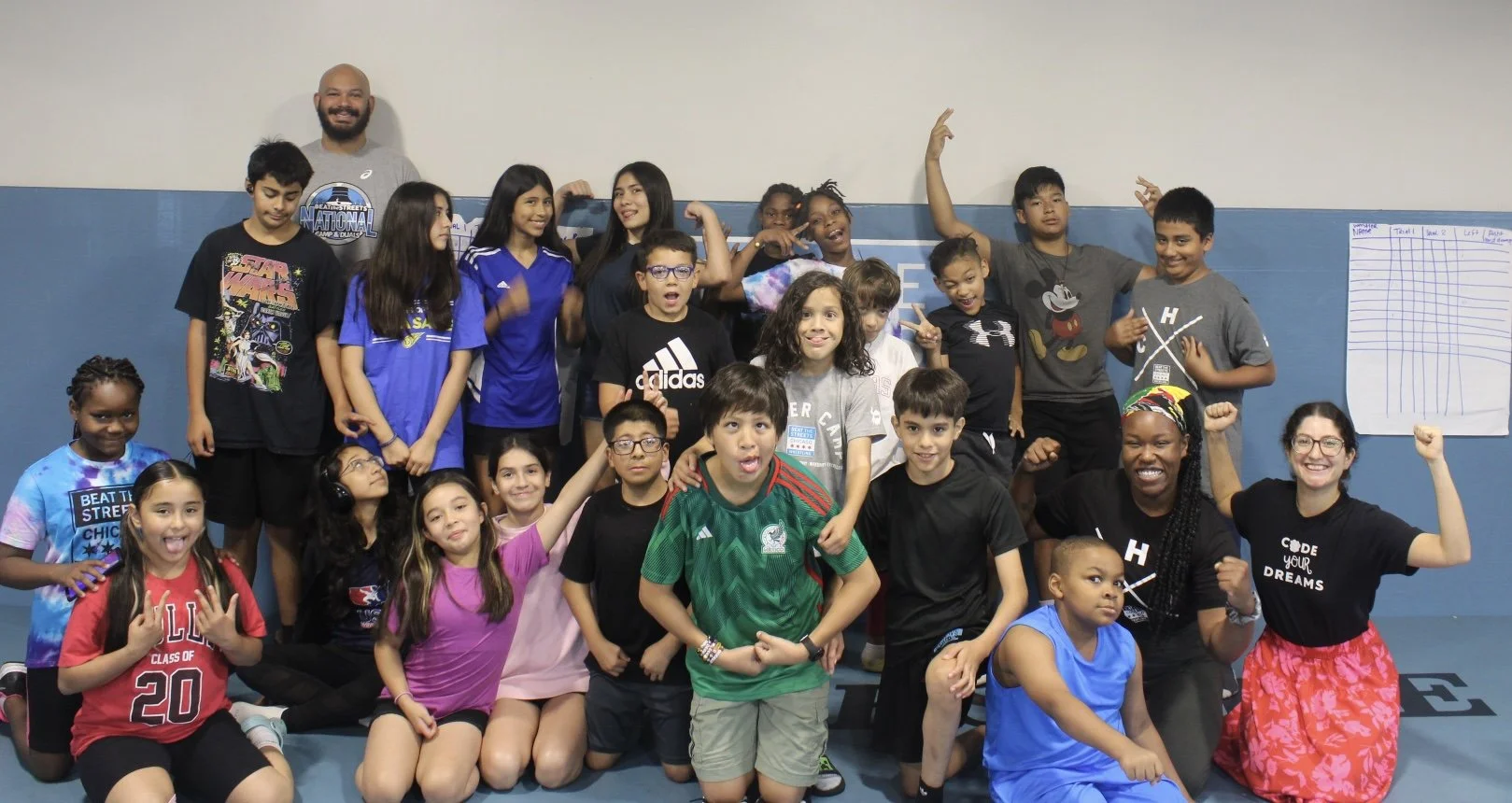 Diverse children and adults posing energetically with raised arms in a gym.