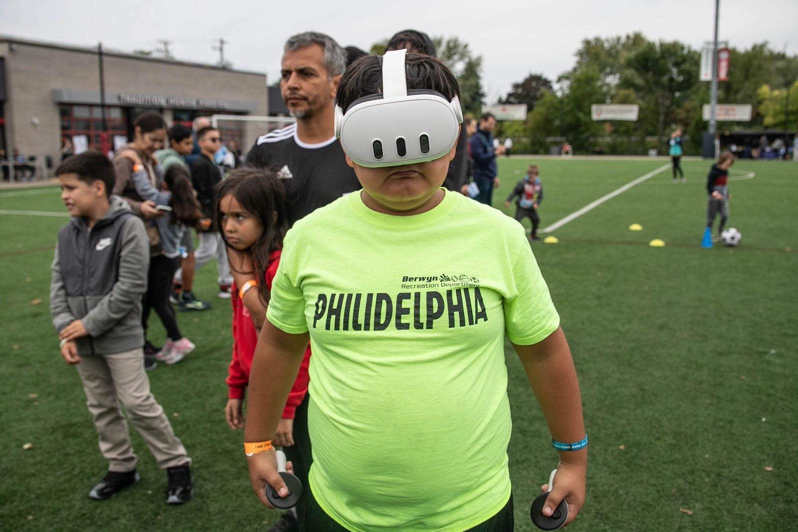 Child in VR headset standing on a soccer field with crowd behind.