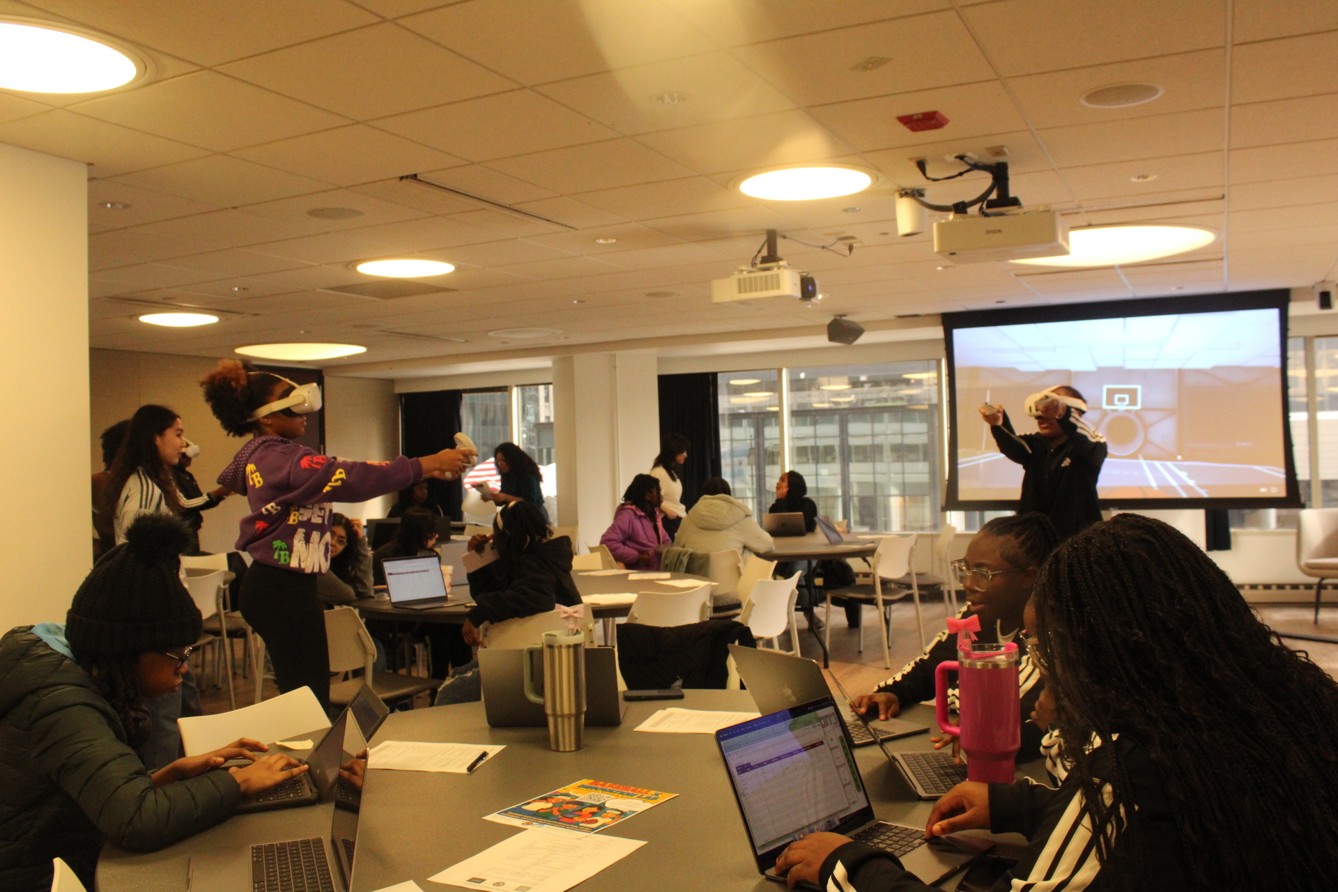 Students on laptops and VR headsets in classroom with basketball on screen.