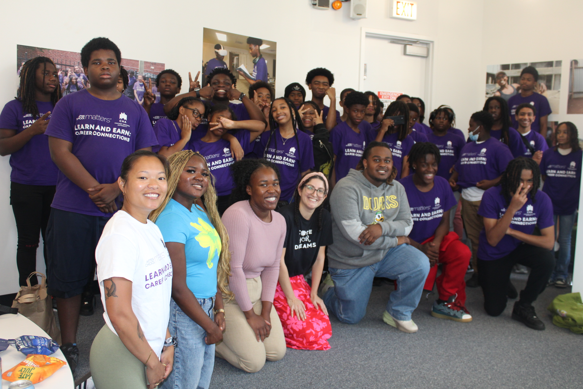 Diverse students and mentors posing in purple shirts in a classroom.