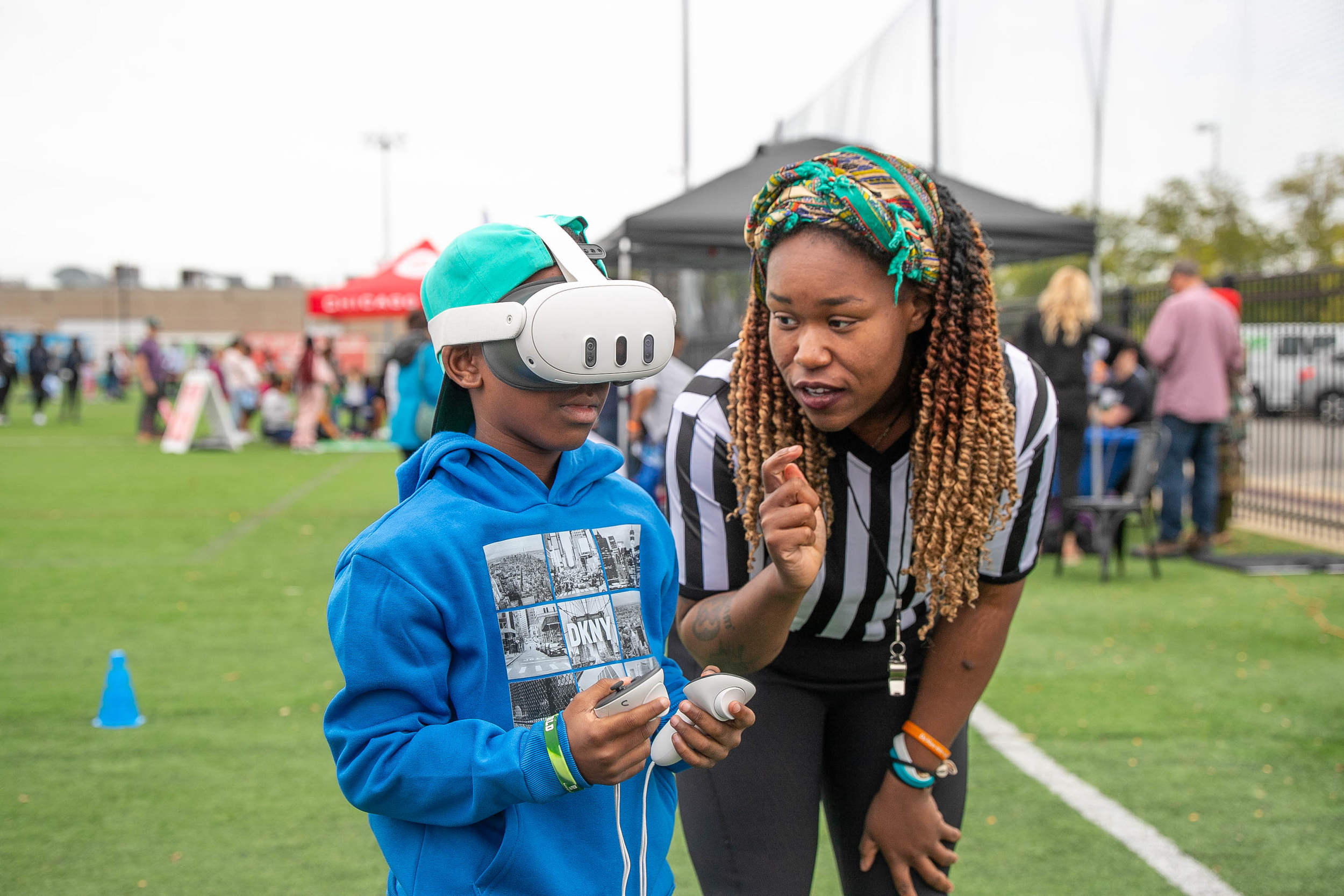 Woman guiding a boy using a VR headset on a sports field.