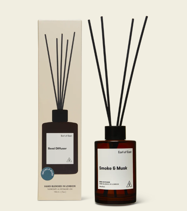 A reed diffuser with black reeds in a brown glass bottle labeled 'Smoke & Musk' and its packaging box.