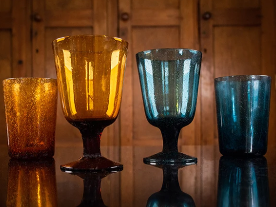 Four colorful glass drinking cups on a reflective surface with a wooden background.