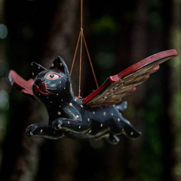 Decorative black cat with wings hanging from a string outdoors.