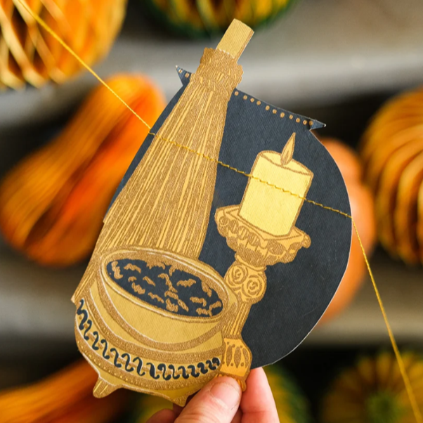 Fall-themed paper decoration featuring a candle on a candlestick, a harvest ladle, and a bundle of wheat.