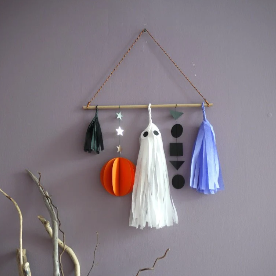 Decorative wall hanging with paper ghosts, stars, planets, and tassels against a purple wall.