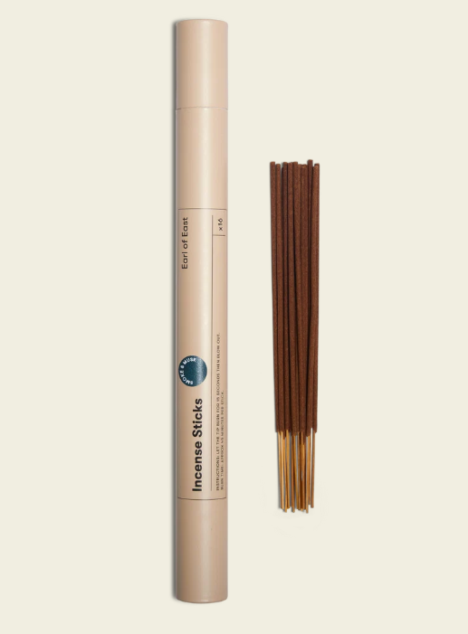 A container of incense sticks with a bundle of brown incense sticks next to it.