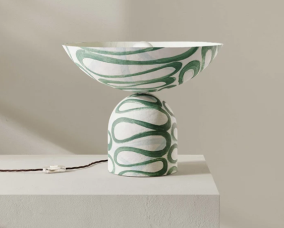 Ceramic table lamp with a green swirling pattern, placed on a white pedestal against a beige wall.