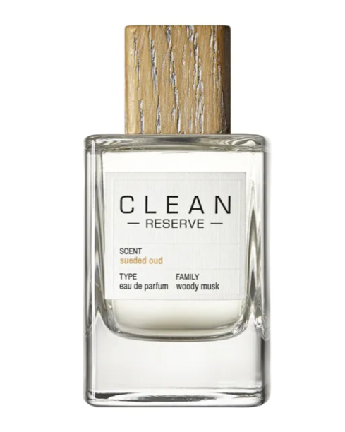 A bottle of perfume labeled 'CLEAN RESERVE,' with a wooden cap and a white label indicating the scent as 'suede oud,' the type as 'eau de parfum,' and the family as 'woody musk.'