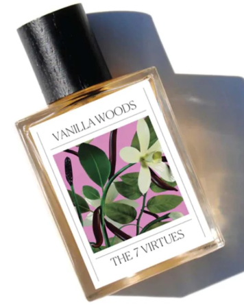 A bottle of Vanilla Woods perfume by The 7 Virtues with a floral label, black cap, and a shadow cast on a surface.