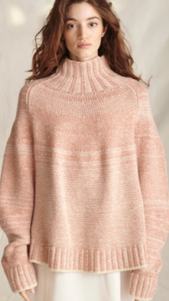 Young woman with long, wavy brown hair wearing a oversized pink knit turtleneck sweater against a neutral background.