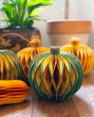 Colorful paper lanterns in orange and green on a wooden table with potted plants in the background.